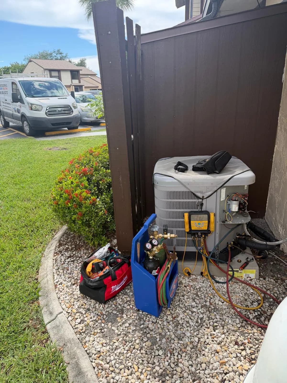 AC Professional technician servicing an outdoor unit with the service van parked behind